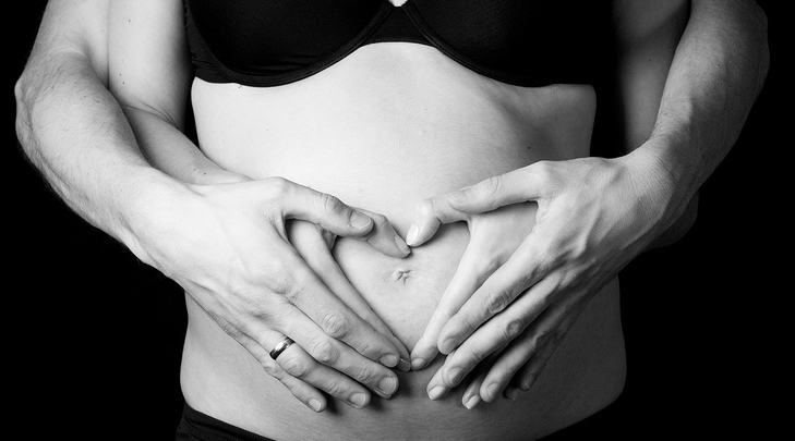 Pregnancy belly with fingers heart symbol. Dark tone.